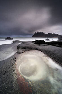 Sturmwolken über der von Wellen umspülten Felsformation The Eye, Uttakleiv, Leknes, Vestvagoy, Nordland, Lofoten, Norwegen, Skandinavien, Europa - RHPLF21762