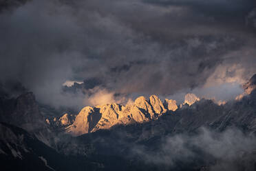 Lichtstrahlen, die bei Sonnenuntergang auf die Berggipfel der Dolomiten treffen, umgeben von niedrigen Wolken und Nebel, Cortina d'Ampezzo, Dolomiten, Venetien, Italien, Europa - RHPLF21785