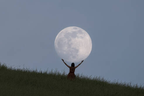 Full moon portrait at blue hour with a girl holding the moon above her head, Emilia Romagna, Italy, Europe - RHPLF21787