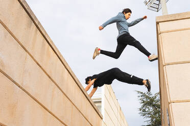 From below side view of full length active men jumping over border roof while training in urban street - ADSF34189