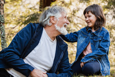 Bearded grandad with charming granddaughter sitting in woods and looking to each other - ADSF34236