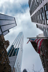 Von unten der zeitgenössischen Hochhäuser mit nationaler amerikanischer Flagge auf der Straße von New York City gegen bewölkten Himmel - ADSF34246