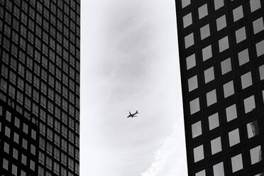 Schwarz und weiß von modernen Flugzeugen fliegen gegen bewölkten Himmel in der Nähe von Hochhäusern auf der Straße von New York City - ADSF34254
