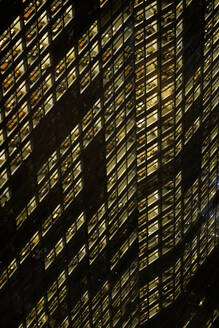 Vollbild eines modernen mehrstöckigen Gebäudes mit leuchtenden Fenstern auf einer dunklen Straße in New York City bei Nacht - ADSF34257