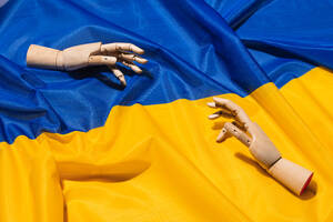 Von oben von hölzernen Schaufensterpuppe Hände greifen für einander auf nationale bunte ukrainische Flagge mit blauen und gelben Farben während des Krieges - ADSF34301