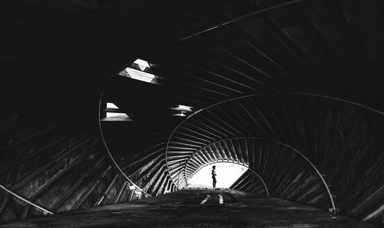 Side view of distant unrecognizable person standing at entrance in spacious round dark tunnel with metal rails and creative design - ADSF34325