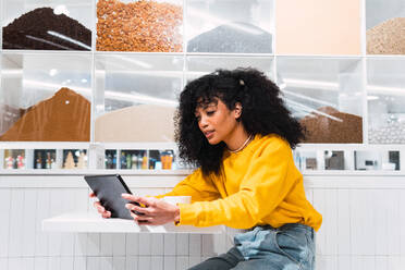 Inhalt Afroamerikanische Frau mit Afrofrisur, die einen Tablet-Computer in der Nähe einer kreativen Wand benutzt - ADSF34360