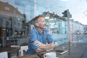 Businessman sitting with arms crossed looking through window at cafe - GUSF07200