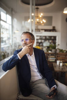 Nachdenklicher Geschäftsmann mit Hand am Kinn in einem Café sitzend - GUSF07206