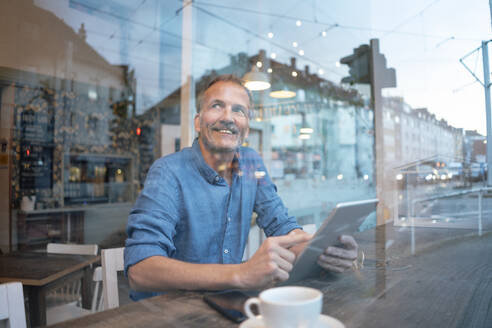 Lächelnder Geschäftsmann sitzt mit Tablet-PC im Café - GUSF07215