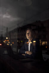 Businessman sitting in dark in cafe at night - GUSF07216