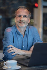 Smiling businessman with laptop sitting at cafe - GUSF07228