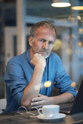 Serious businessman with hand on chin sitting at table in cafe - GUSF07229