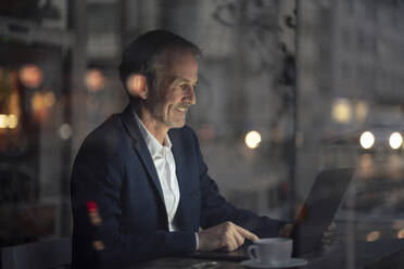 Smiling freelancer working on laptop in cafe at night - GUSF07237