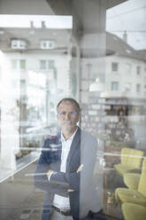 Businessman with arms crossed seen through glass window at cafe - GUSF07251