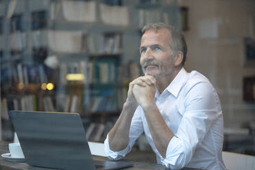 Businessman with hand on chin sitting by glass window at cafe - GUSF07284