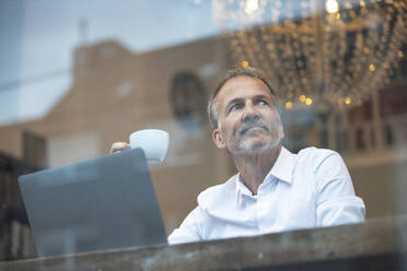 Businessman with coffee cup and laptop sitting in cafe - GUSF07285