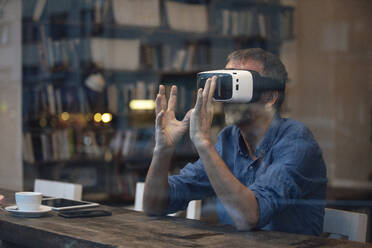 Geschäftsmann, der einen Virtual-Reality-Simulator trägt und am Tisch sitzt - GUSF07295