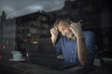 Geschäftsmann mit Laptop bei der Arbeit in einem Café bei Nacht - GUSF07302