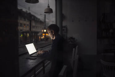 Geschäftsmann arbeitet im Dunkeln an einem Laptop in einem Café - GUSF07304