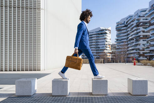 Businessman holding shoulder bag walking on concrete block - OIPF01444