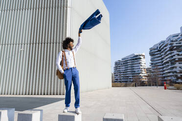 Carefree businessman waving blazer standing on concrete block - OIPF01450