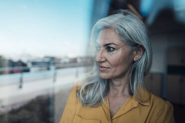 Thoughtful businesswoman with gray hair seen through glass - JOSEF08298