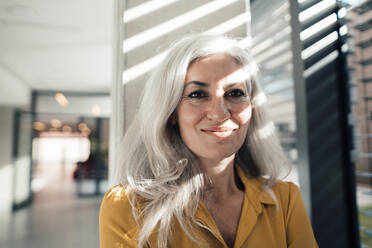 Smiling woman standing in front of column at work place - JOSEF08324