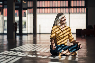 Smiling business person sitting with cross-legged in office - JOSEF08327