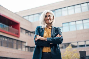 Businesswoman standing with arms crossed outside office building - JOSEF08330