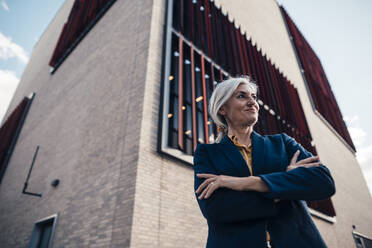 Smiling businesswoman standing with arms crossed in front of office building - JOSEF08346