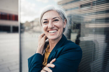 Cheerful businesswoman with gray hair by glass wall - JOSEF08360