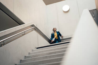 Businesswoman with laptop standing at staircase - JOSEF08369