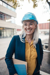 Cheerful engineer wearing with clipboard standing at office park - JOSEF08376