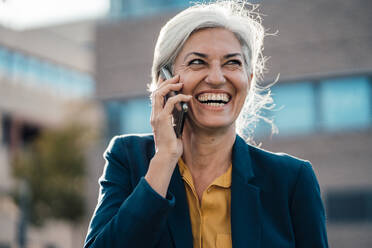 Cheerful businesswoman with gray hair talking on smart phone - JOSEF08386