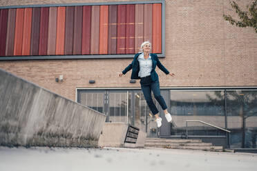 Geschäftsfrau springt vor einem Bürogebäude - JOSEF08392