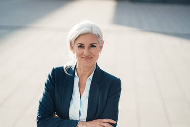 Smiling businesswoman standing with arms crossed on sunny day - JOSEF08394