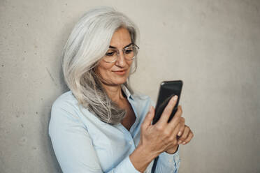Geschäftsfrau mit Brille und Mobiltelefon vor einer Wand - JOSEF08436