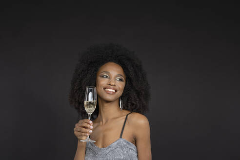 Smiling young woman holding champagne flute against black background - EIF03599