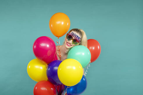 Lächelnde junge Frau mit Geburtstagsbrille hält Luftballons vor grünem Hintergrund - EIF03623