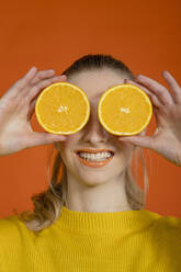 Lächelnde junge Frau, die ihre Augen mit einer Orangenscheibe bedeckt - EIF03631