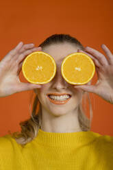 Smiling young woman covering eyes with slice of oranges - EIF03631