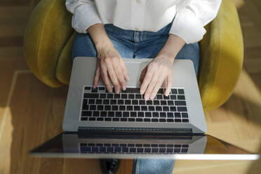Hands of woman using laptop sitting on armchair - OGF01118