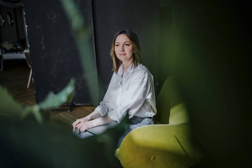 Smiling woman with laptop sitting on armchair - OGF01119