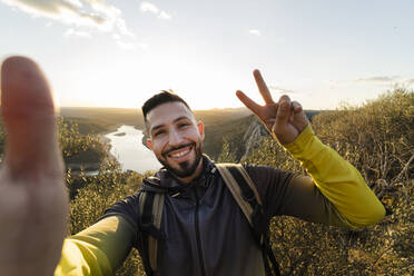 Männlicher Wanderer macht eine Friedensgeste, während er ein Selfie im Monfrague National Park macht - JCCMF05870