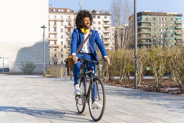 Glücklicher Geschäftsmann mit Umhängetasche auf dem Fahrrad auf dem Fußweg - OIPF01459