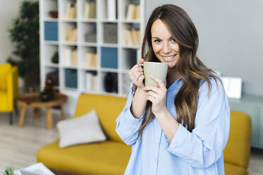 Lächelnde junge Frau mit Kaffeetasse zu Hause - GIOF15004