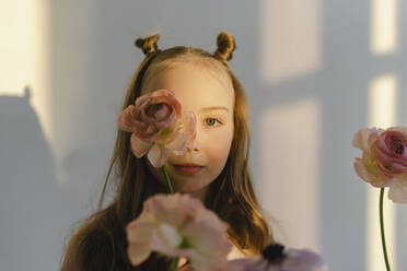 Nettes Mädchen mit Blume im Gesicht an einer weißen Wand stehend - SEAF00740