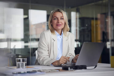 Lächelnde Geschäftsfrau mit Laptop am Schreibtisch im Büro - RBF08791