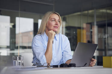 Businesswoman with hand on chin at desk in office - RBF08794
